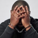 Handcuffs, arrested criminal and black man with stress, worry and anxiety in police station for crime. Law, punishment and male person with chains for investigation, theft and fraud suspect in prison