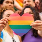 A group of LGBTQ people holding a rainbow heart celebrating International Pride Month.