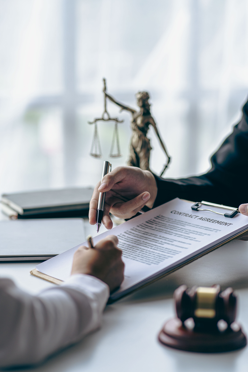 Business lawyers working on law in a courtroom help clients read legal documents and study information about court cases, along with a justice scale and hammer.